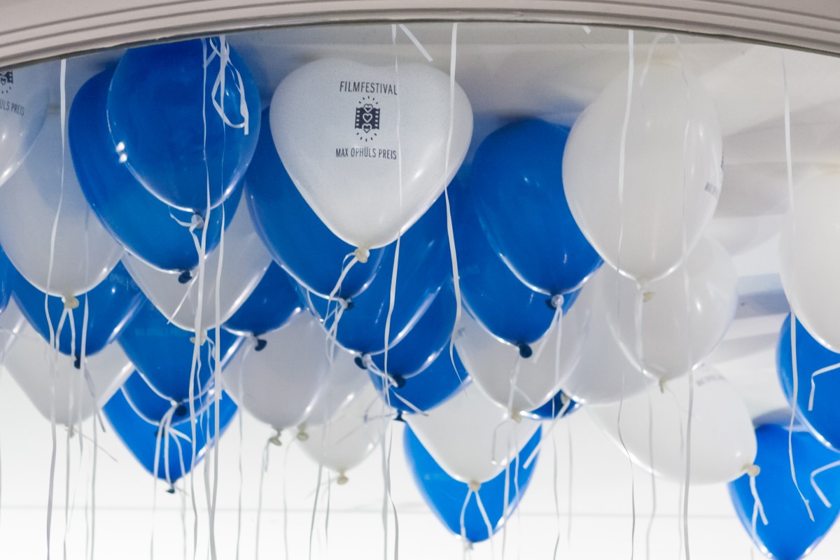 Blau-weiße Ballons mit Aufdruck »Filmfestival Max Ophüls Preis«, die von der Decke hängen, mit weißen Schnüren befestigt.