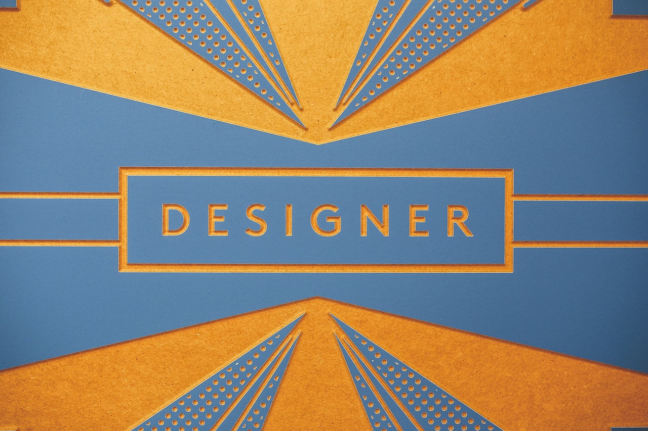 Das Bild zeigt eine stilisierte Grafik mit dem Wort "DESIGNER" in großen Buchstaben. Die Farben Blau und Orange dominieren das Design, das geometrische Muster und feine Details im Art-Deco-Stil verwendet.