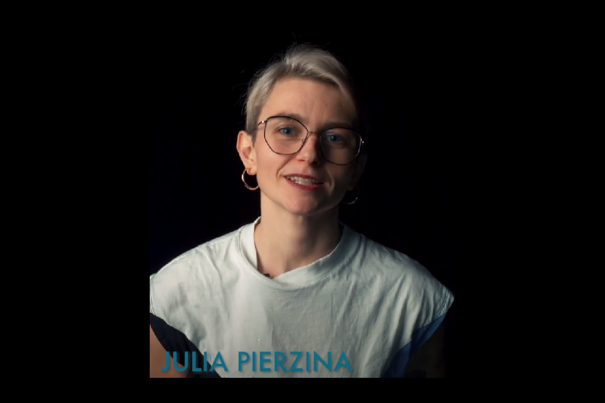 „Eine Person mit kurzem blondem Haar, Brille und Ohrringen trägt ein helles Shirt und spricht vor einem dunklen Hintergrund. Unten im Bild steht der Name »Julia Pierzina« in blauer Schrift.“