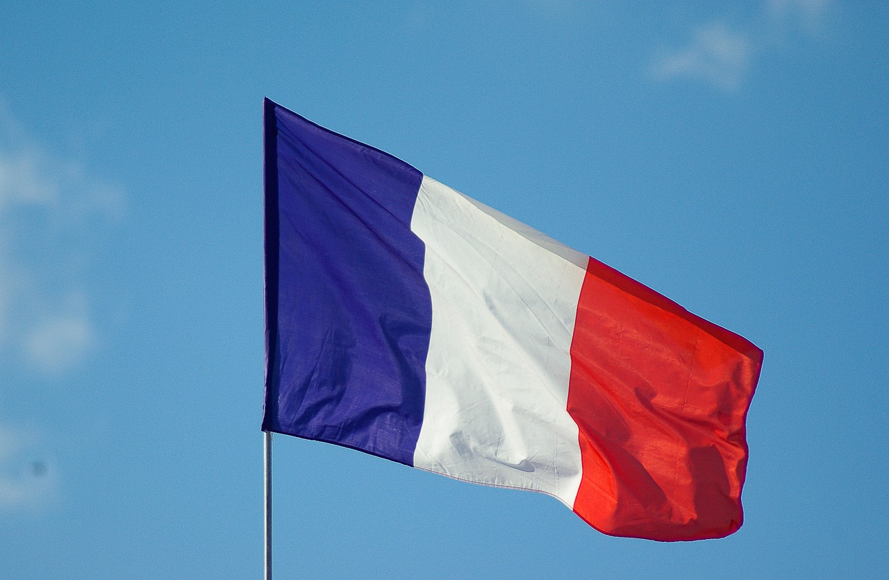 Die französische Flagge mit den Farben Blau, Weiß und Rot weht an einem Fahnenmast vor einem blauen Himmel.
