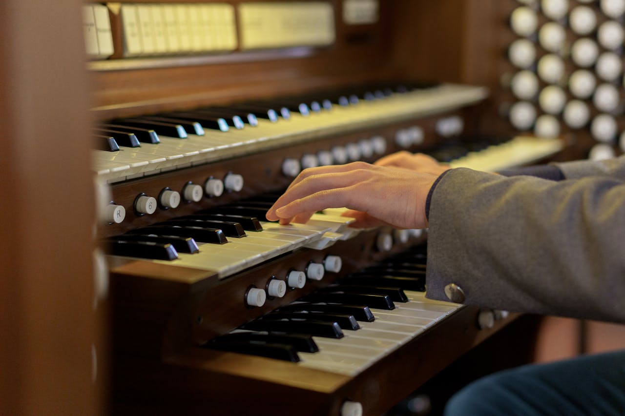 Eine Nahaufnahme von Händen, die auf den Tasten einer Kirchenorgel spielen. Die Orgel hat mehrere Tastenreihen und zahlreiche Knöpfe zur Klangsteuerung.