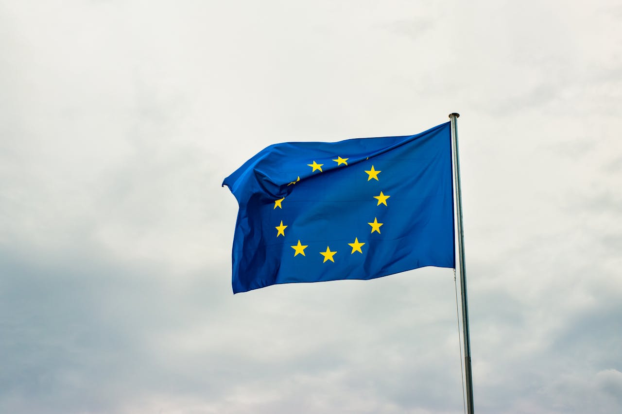 Eine Europaflagge mit zwölf goldenen Sternen auf blauem Hintergrund weht im Wind vor einem bewölkten Himmel.