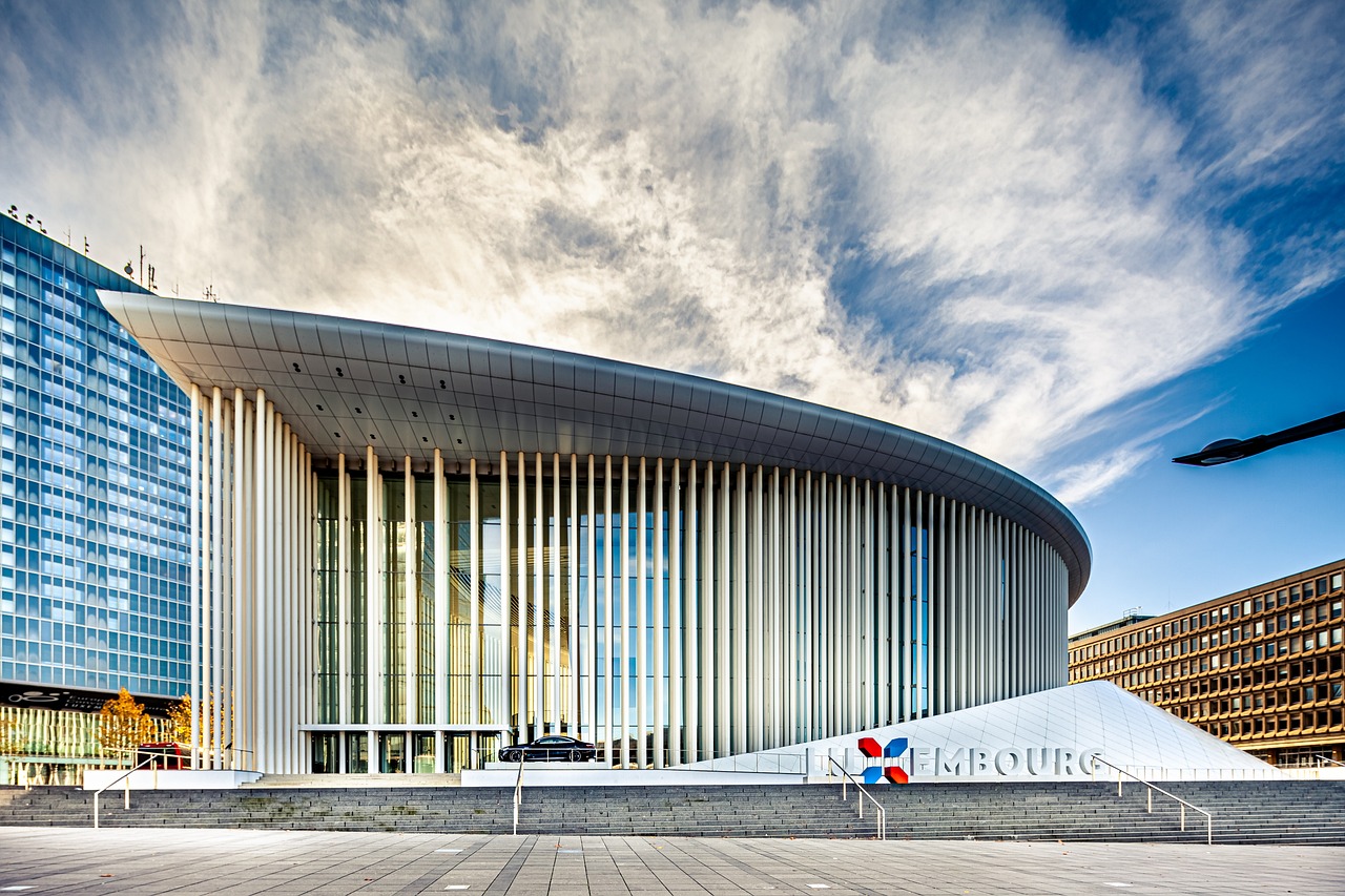 Außenansicht der Philharmonie Luxemburg mit ihrer modernen Architektur, großen Glasfassade und markanten weißen Säulen vor blauem Himmel.