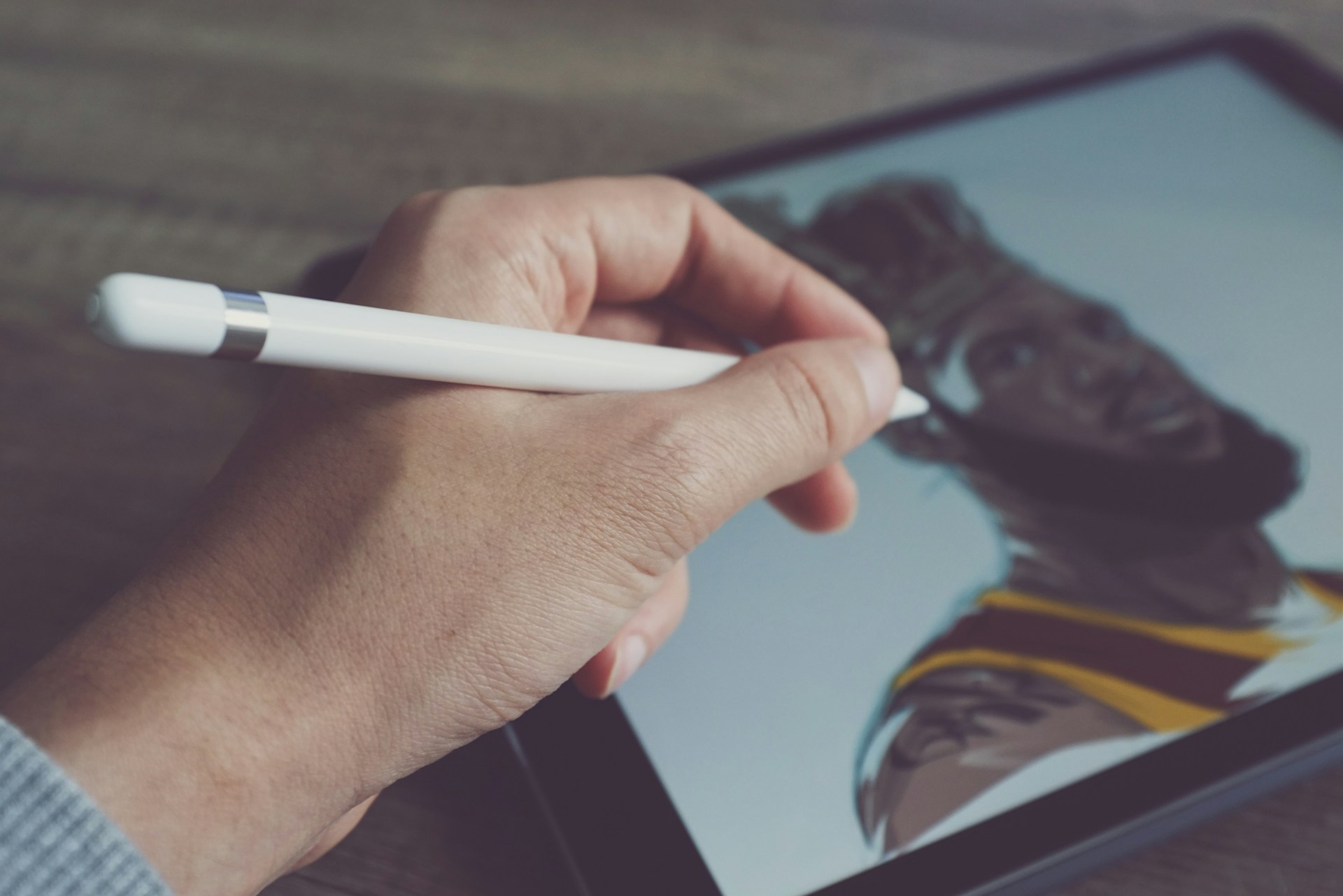 Eine Hand hält einen digitalen Eingabestift und zeichnet auf einem Tablet ein Porträt eines Mannes mit Bart und Basketballtrikot.