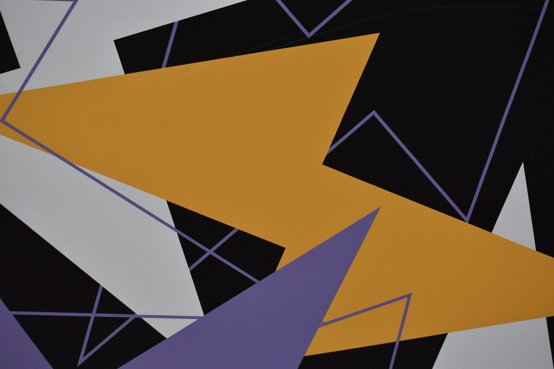 Abstraktes Kunstwerk mit überlappenden geometrischen Formen in Schwarz, Weiß, Senfgelb und Violett. Die Formen bestehen aus scharfen Dreiecken und Linien, die ein dynamisches, energiegeladenes Muster erzeugen.