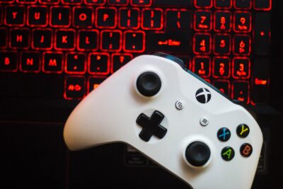 Ein weißer Xbox-Controller liegt auf der Tastatur eines Laptops mit rot beleuchteten Tasten. Die Szene betont den Gaming-Aspekt und die Verbindung zwischen Konsole und PC.