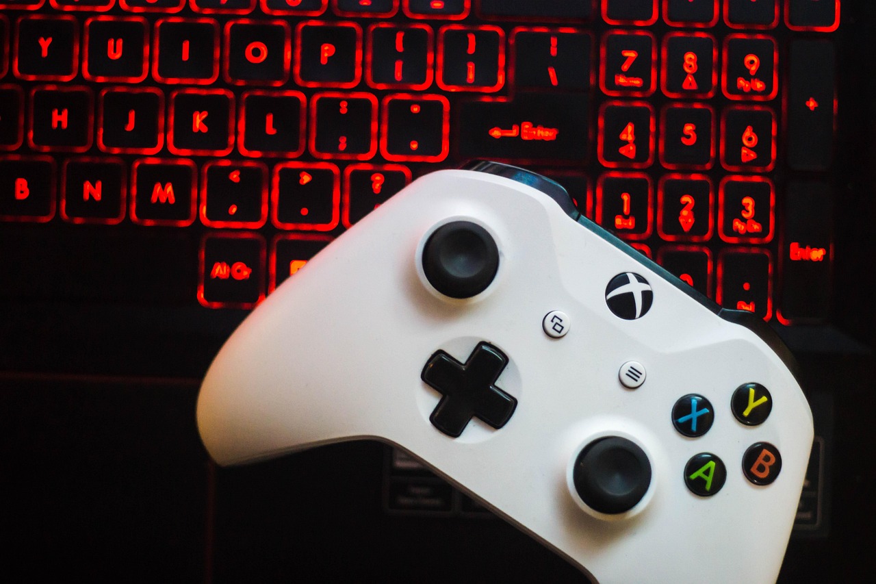 Ein weißer Xbox-Controller liegt auf der Tastatur eines Laptops mit rot beleuchteten Tasten. Die Szene betont den Gaming-Aspekt und die Verbindung zwischen Konsole und PC.