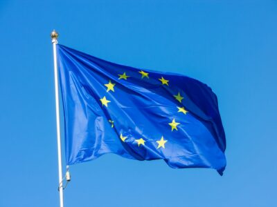 Eine wehende Flagge der Europäischen Union mit zwölf gelben Sternen auf blauem Hintergrund, aufgenommen vor einem klaren, blauen Himmel.