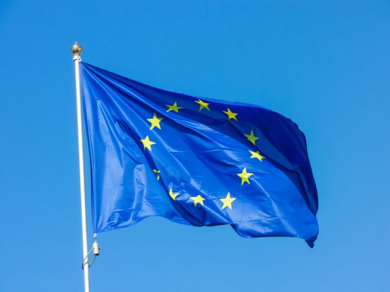 Eine wehende Flagge der Europäischen Union mit zwölf gelben Sternen auf blauem Hintergrund, aufgenommen vor einem klaren, blauen Himmel.