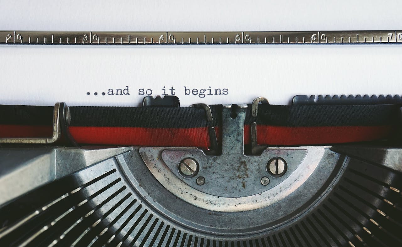 Nahaufnahme einer Schreibmaschine, die auf ein Blatt Papier den Satz „...and so it begins“ tippt.
