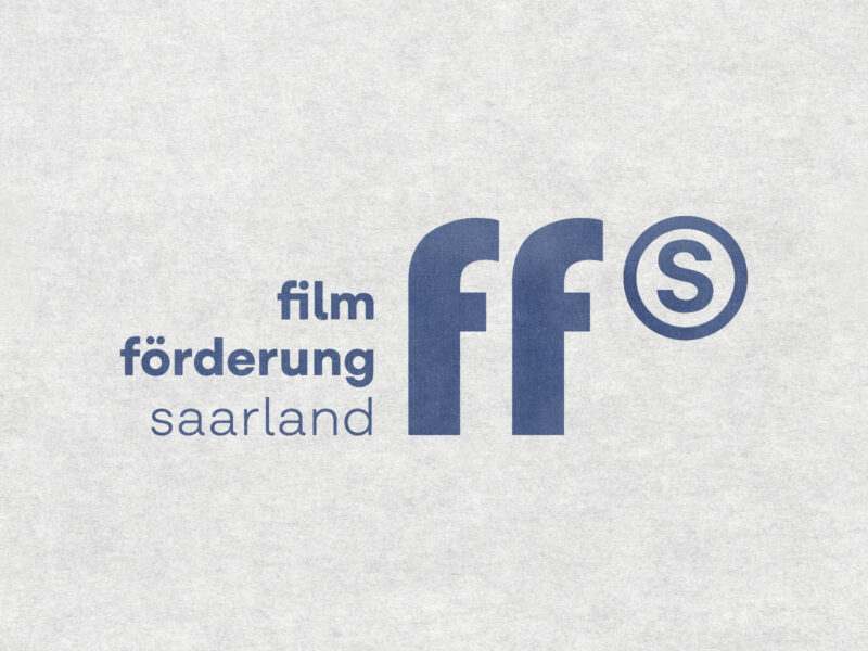 Logo der Filmförderung Saarland auf hellem, leicht strukturiertem Hintergrund. Links steht der ausgeschriebene Name „film förderung saarland" in dunkelblauer Schrift, rechts daneben das grafische Kürzel „ffs": zwei große, stilisierte Kleinbuchstaben „f" sowie ein eingekreistes „S", alles in derselben dunkelblauen Farbe.