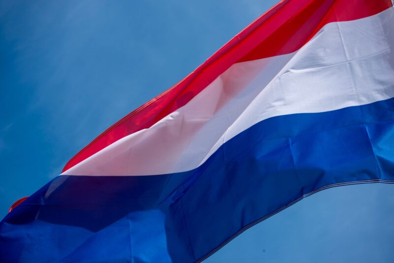 Die luxemburgische Flagge weht im Wind vor blauem Himmel. Die Fahne zeigt die drei horizontalen Streifen in Rot, Weiß und Blau und ist durch den Wind in Bewegung, sodass sich Falten und Wellen im Stoff abzeichnen.