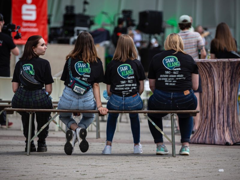 Saarklang Festival: Das Bild zeigt die Rücken einiger Teammitglieder, die auf einer Bank sitze.
