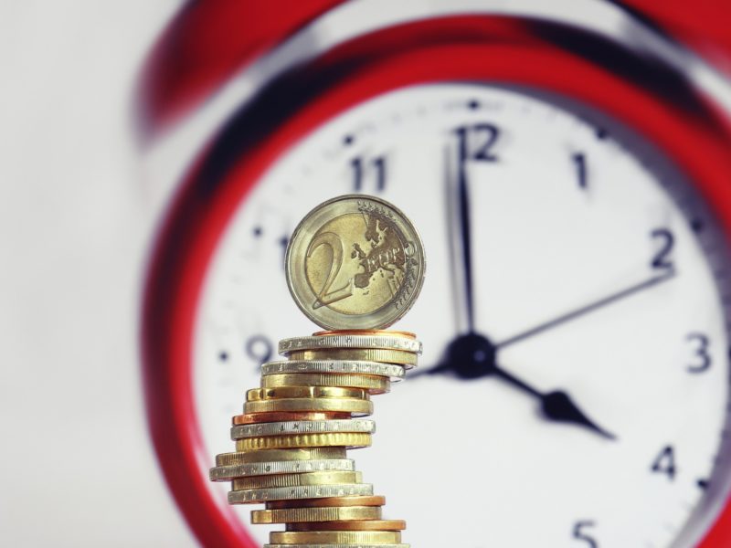 Stundensatz ist kein Stundenlohn: Symbolmotiv Wecker mit aufgestapelten Münzen