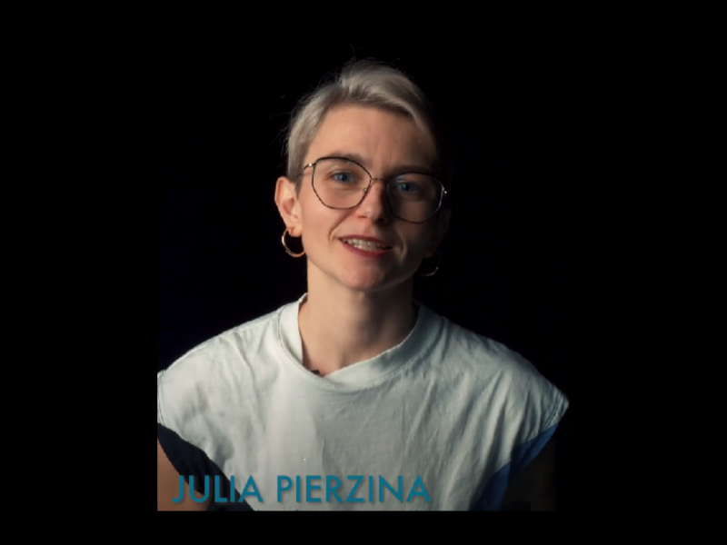 „Eine Person mit kurzem blondem Haar, Brille und Ohrringen trägt ein helles Shirt und spricht vor einem dunklen Hintergrund. Unten im Bild steht der Name »Julia Pierzina« in blauer Schrift.“