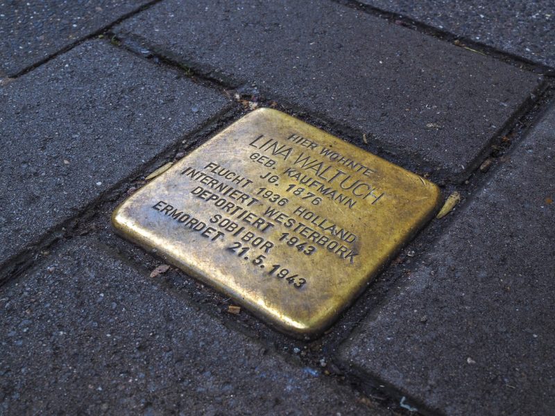 Ein Stolperstein aus Messing ist in den Gehweg eingelassen. Die Gravur zeigt den Namen Lina Waltuch, geboren 1876. Der Text beschreibt ihre Flucht nach Holland, Internierung in Westerbork und Deportation nach Sobibor, wo sie am 21. Mai 1943 ermordet wurde.