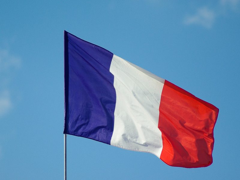 Die französische Flagge mit den Farben Blau, Weiß und Rot weht an einem Fahnenmast vor einem blauen Himmel.