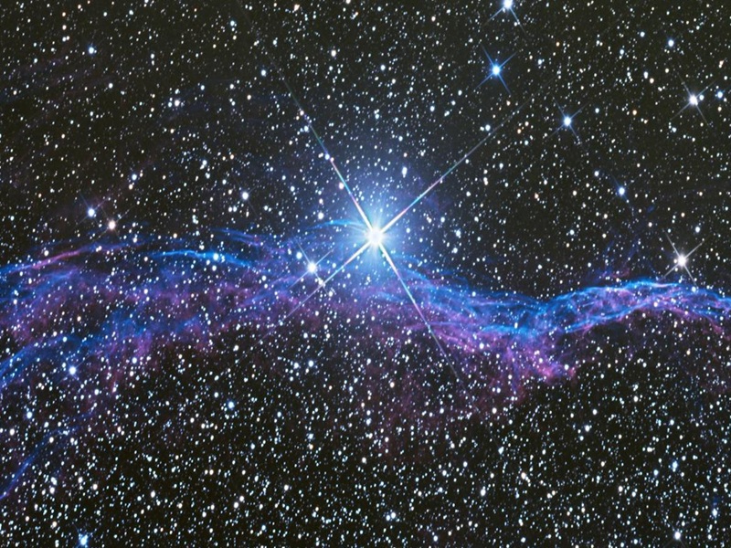 Ein funkelnder Sternenhimmel mit einem strahlend hellen Stern im Zentrum. Um den Stern herum sind violette und blaue, wolkenartige Strukturen zu sehen, die an einen kosmischen Nebel erinnern. Der Hintergrund ist tiefschwarz mit zahlreichen kleineren Sternen, die den Himmel bedecken.