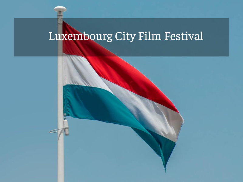 Die Nationalflagge von Luxemburg weht an einem Fahnenmast vor blauem Himmel. Über dem Bild liegt ein transparenter Banner mit der Aufschrift „Luxembourg City Film Festival“.