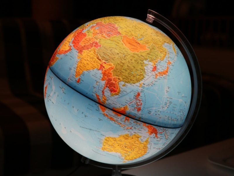 Ein beleuchteter Globus mit Fokus auf Asien, Australien und dem Indischen Ozean. Der Globus steht in einem dunklen Raum auf einem Tisch, im Hintergrund ist ein gestreiftes Sofa zu erkennen.