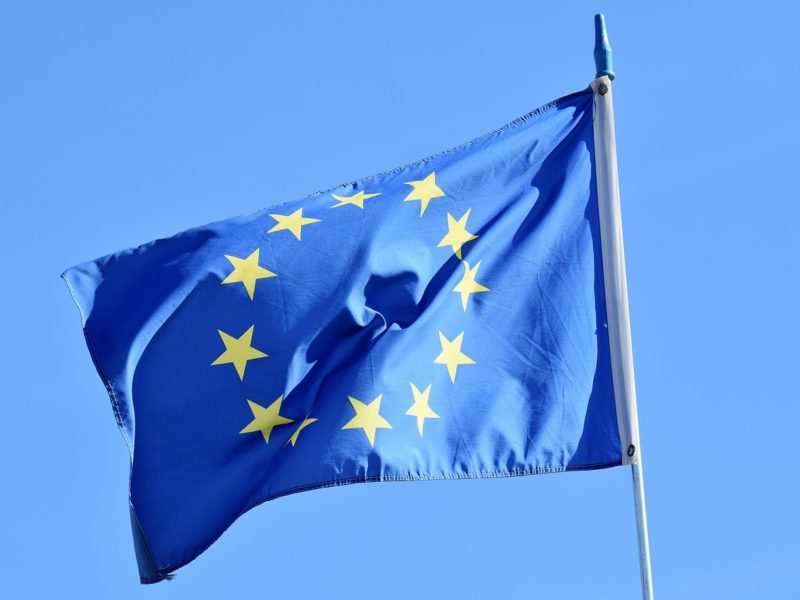 Eine wehende Europaflagge mit zwölf goldenen Sternen auf blauem Grund, aufgenommen vor einem klaren, blauen Himmel.