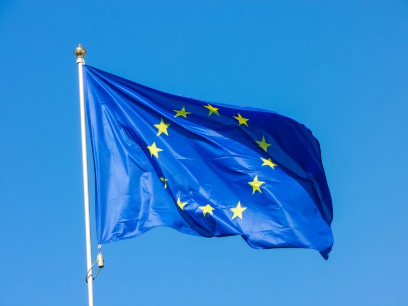 Eine wehende Flagge der Europäischen Union mit zwölf gelben Sternen auf blauem Hintergrund, aufgenommen vor einem klaren, blauen Himmel.