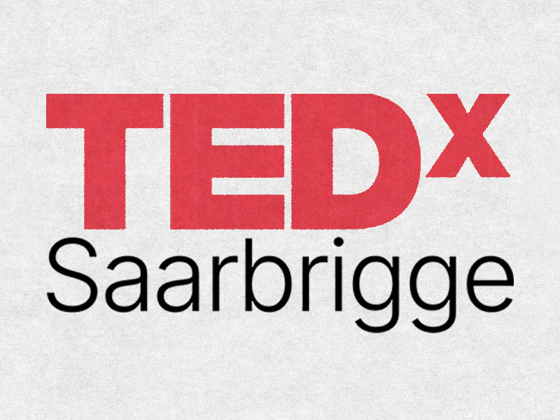 Auf dem Bild ist ein klar strukturiertes Logo zu sehen, das an das bekannte Erscheinungsbild von TEDx-Veranstaltungen angelehnt ist. Der obere Teil zeigt in kräftigem Rot den Schriftzug „TEDx“, wobei das „x“ deutlich kleiner gesetzt ist und rechts neben dem Hauptschriftzug steht. Darunter folgt in schwarzer Schrift der Ortsname „Saarbrigge“, der in einer modernen, gut lesbaren Typografie gestaltet ist. Der Hintergrund besteht aus einer hellen, leicht texturierten Fläche, die das Logo ruhig und aufgeräumt wirken lässt. Insgesamt vermittelt das Bild den Eindruck einer eigenständigen, lokal verankerten TEDx-Edition, die professionell und gleichzeitig nahbar wirkt.